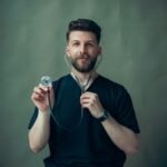 Portrait of a young male doctor with a stethoscope, wearing a black t-shirt.