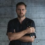 Portrait of a confident doctor standing with a stethoscope against a plain background, symbolizing medical professionalism.